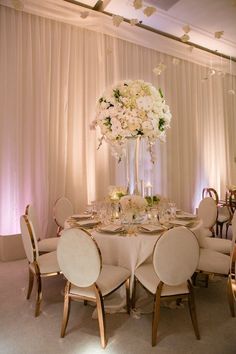 a table with white chairs and flowers in a vase on the top is set up for a formal function