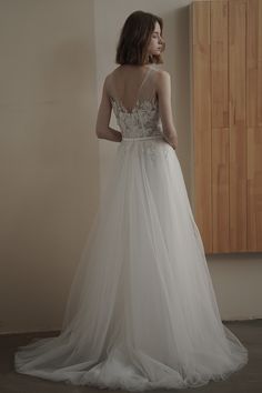 a woman standing in front of a window wearing a wedding dress with an open back