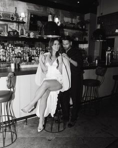 a woman sitting on a stool in front of a bar while a man combs her hair