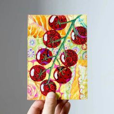 a hand holding up a piece of art with red cherries on it and green stems