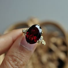 a woman's hand holding a ring with a large red stone in the middle