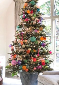 a brightly colored christmas tree in a living room next to a large window with curtains