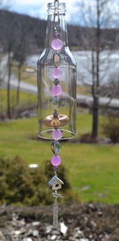 a glass jar with beads hanging from it's side in front of a grassy area