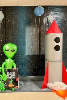 a green alien is standing next to a rocket