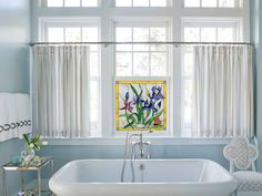 a bath tub sitting next to a window in a bathroom with blue walls and white curtains