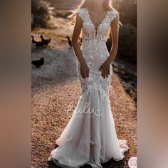 a woman in a white wedding dress standing on a dirt road with chickens behind her