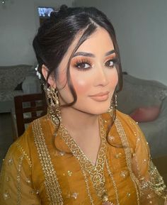 a woman with long hair wearing earrings and a yellow dress sitting in front of a couch