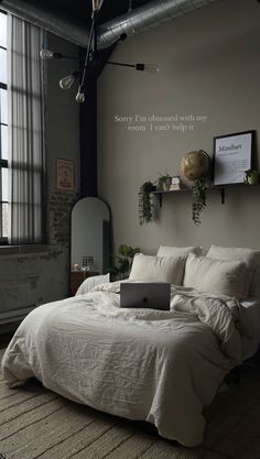 a laptop computer sitting on top of a white bed in a room with high ceilings