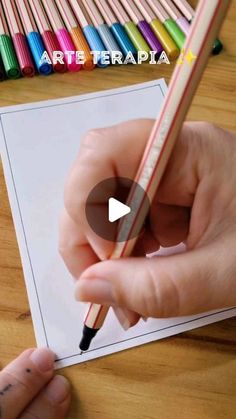 a person holding a pencil in their hand and drawing on paper with colored crayons behind them