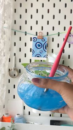 a person holding a toothbrush in a jar filled with blue liquid on a shelf