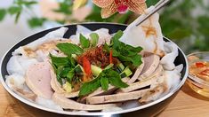 a bowl filled with meat and vegetables on top of a wooden table next to flowers