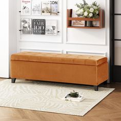 an orange bench sitting on top of a rug in front of a white wall with pictures