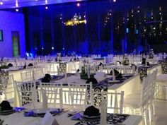 tables and chairs are set up with white linens, black napkins, and blue lights