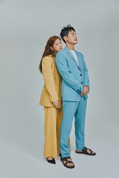 a man and woman standing next to each other in front of a gray background wearing blue suits