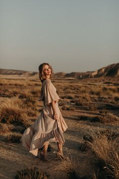 a woman in a dress walking through the desert