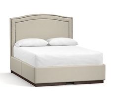 an upholstered bed with white sheets and pillows