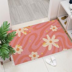 a door mat with flowers on it next to a potted plant and white slippers