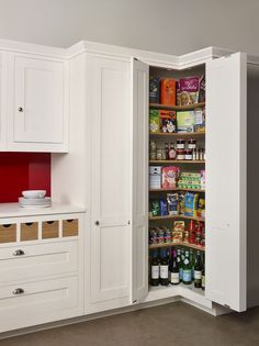 an open pantry door in a kitchen with white cabinets and cupboards filled with food