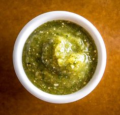 a white bowl filled with green sauce on top of a wooden table