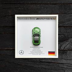 a green car in a white frame on a wooden surface with the mercedes logo above it