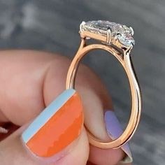 a woman's hand holding an orange and blue ring with a diamond on it