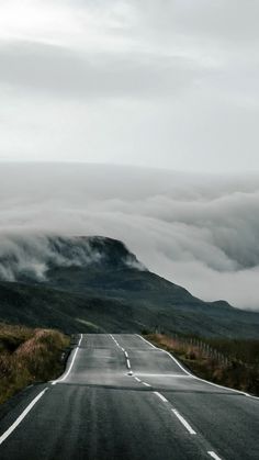 an empty road in the middle of nowhere with low lying clouds on it's sides