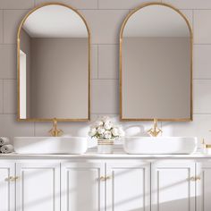 two sinks and mirrors in a bathroom with gold trim on the wall, along with white cabinets