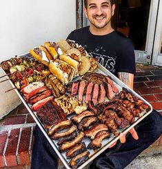 a man is holding a tray full of meats and sausages on the grill