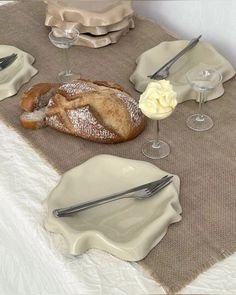 a table set with bread, wine glasses and silverware on top of a cloth