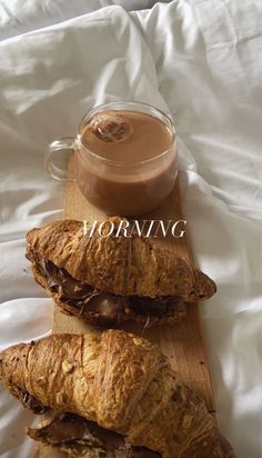 two croissants on a cutting board next to a cup of chocolate milk