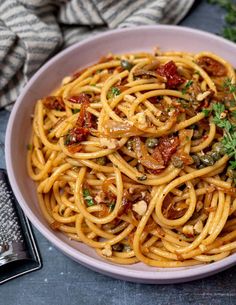 a white bowl filled with pasta and sauce on top of a wooden table next to a fork