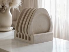 a stack of white plates sitting on top of a counter next to a vase with flowers