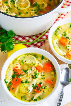 two bowls of chicken noodle soup with lemons and parsley on the side