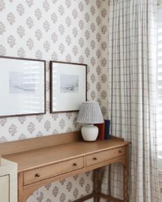 a wooden desk sitting next to a window with two pictures hanging on the wall above it