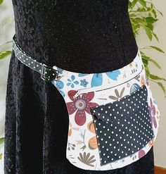 a woman wearing a black dress with white polka dots and flowers on it, holding a multicolored patchwork purse