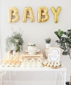 a baby shower party with gold balloons and desserts on a white table next to a potted plant