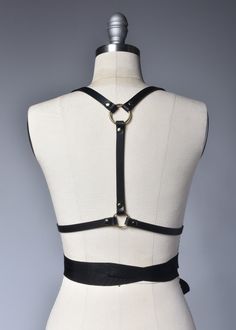 High quality, durable-yet-delicate bespoke harness made in thick PVC or black leather. Fancy, tassel trimmed grosgrain ribbons wrap around the waist and tie into a bow. Fit is adjustable with buckles and straps. The waist is also extremely adjustable due to the ribbon ties. Silver or gold-toned nickel plated steel hardware. Color shown is "Black PVC/Gold Hardware" and "Black Leather/Gold Hardware". Both available with silver tone hardware.All pieces are MADE TO ORDER, standard sizes XS-4XL. If y Elegant Fitted Black Harness, Adjustable Harness For Festival, Fitted Leather Harness With Belt, Leather Strapped Harness, Gothic Leather Harness With Belt, Adjustable Leather Harness With Belt, Fitted Black Strapped Harness, Fitted Leather Harness With Straps, Black Leather Harness With Adjustable Strap