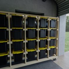 several black and yellow bins are stacked on wooden shelves in front of a grassy area