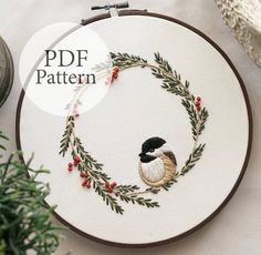 a cross stitch pattern with a bird sitting on it's back in a circle surrounded by greenery