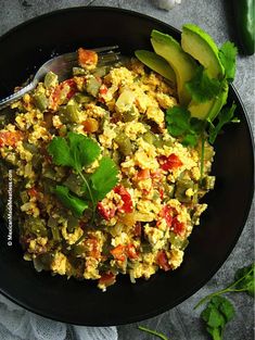 a black plate topped with scrambled eggs and vegetables