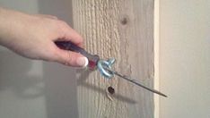 a person holding a pair of pliers in front of a wood paneled wall