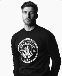 a man standing in front of a white background wearing a manchester city sweatshirt and jeans