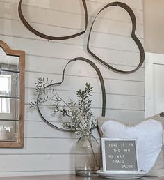 a heart shaped metal wall hanging on the side of a white wooden wall next to a vase filled with flowers