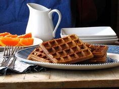 two waffles on a plate with orange slices next to it and a white pitcher