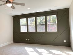 an empty room with three windows and a ceiling fan in the corner, all painted green