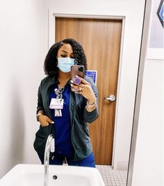 a woman wearing a face mask taking a selfie in front of a bathroom sink