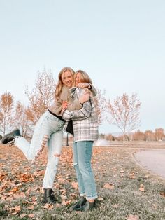 two young women hugging each other in the grass with leaves on the ground behind them