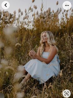 a woman in a blue dress is sitting on the grass and looking up at something