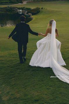 a bride and groom walking in the grass holding hands