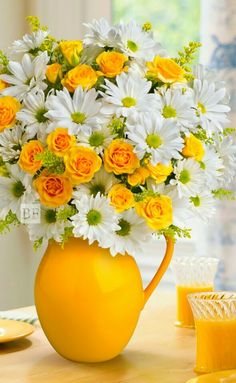 a yellow pitcher filled with lots of white and yellow flowers on top of a table